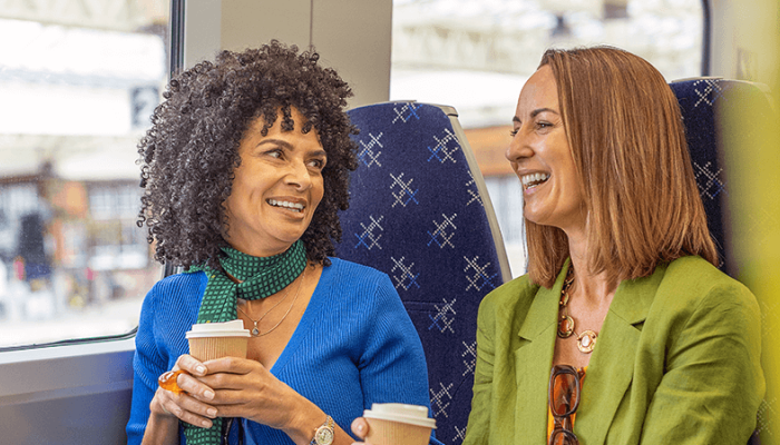 Two females travelling on a ScotRail train, smiling at each other and drinking coffee