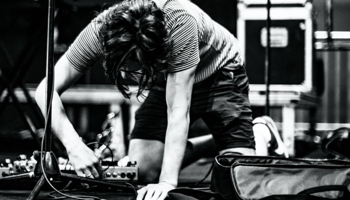 Black and white image of a person plugging in a pedalboard on stage