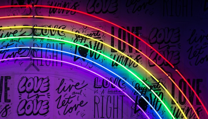 A neon rainbow sign with black writing behind it