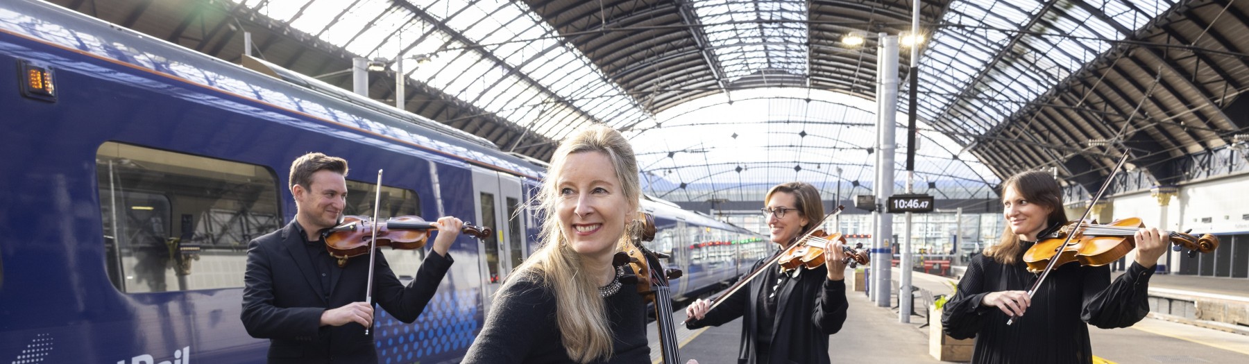 A string quartet plays beside a ScotRail train at a platform in Queen St Station