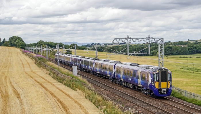A Class 385 train passes by a field of crops in mid-Summer.