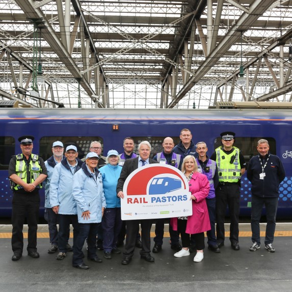 A group of people holding a Rail Pastors Initiative banner standing in front of a ScotRail train at Glasgow Central station 