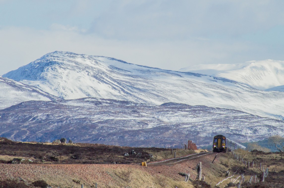 A remote moorland scene with snowcapped hills and a ScotRail train in the distance.