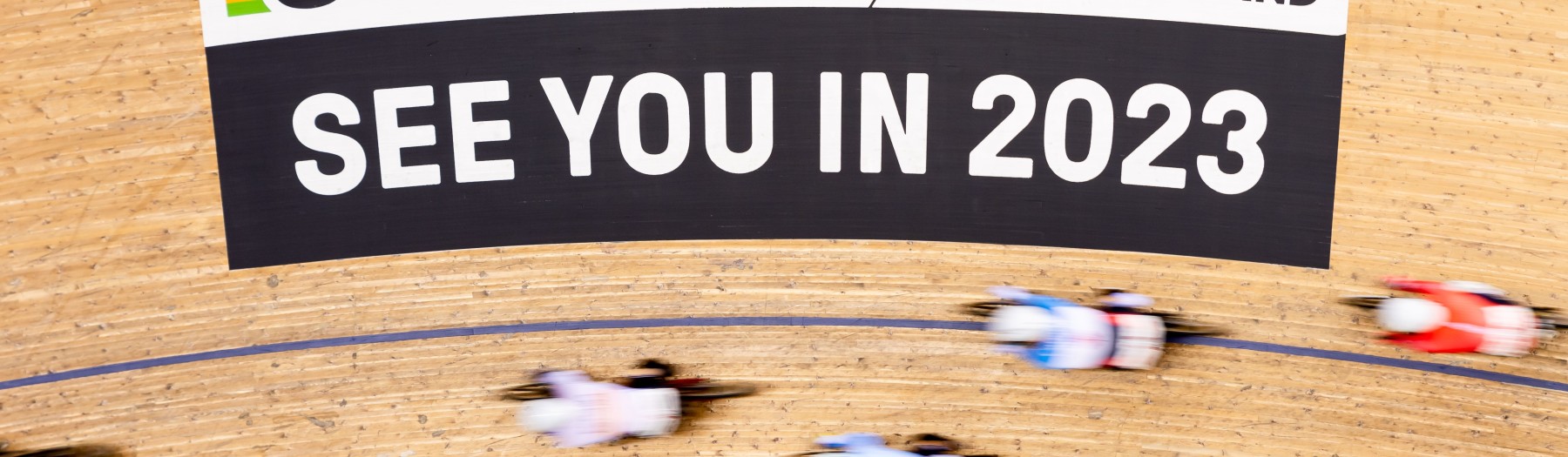 Aerial shot of cyclists on the bend of a track. An advertisement can be seen which reads: "See you in 2023" 