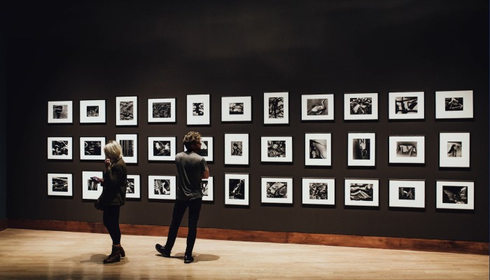 Framed photographs on a dark wall with two people looking at them