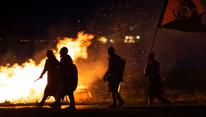 Silhouette of Vikings walking across a backdrop of flames 