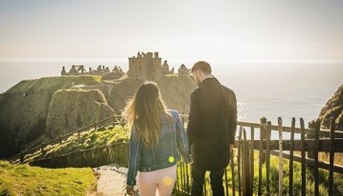 Couple holding hands walking towards Dunnottar Castle near Stonehaven