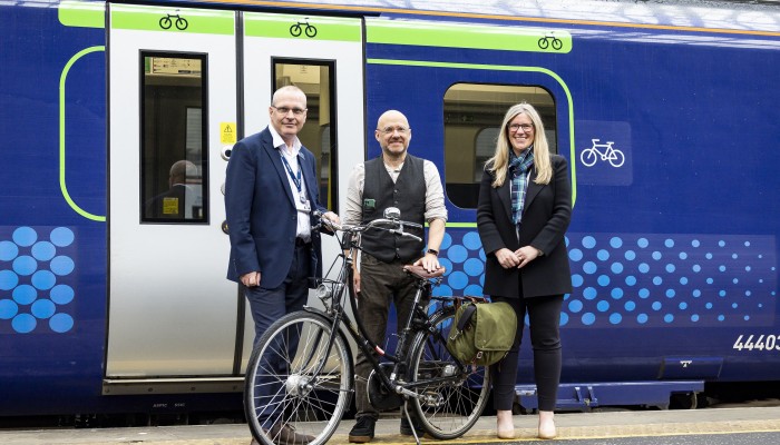 David Lister, ScotRail Safety, Engineering, and Sustainability Director; Patrick Harvie MSP, Minister for Active Travel; Trudy Lindblade, Chief Executive Officer, 2023 UCI Cycling World Championships with a bike in front of bright green signage on a ScotRail train showing where cyclists can board.