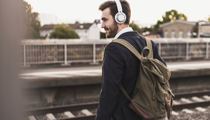 Man standing at bridge wearing backpack and headphones. 