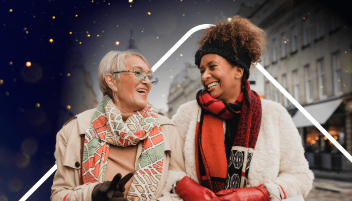 Two ladies walking down the street, smiling at each other, carrying Christmas shopping. There is a ticket device illustration and sparkles in the background behind them. 
