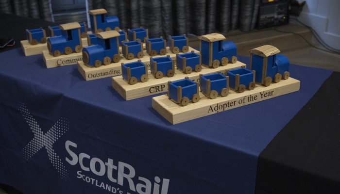 Five ScotRail in the Community Awards sitting on a table draped with a blue ScotRail table cloth. Awards are made of wood and look like blue trains.