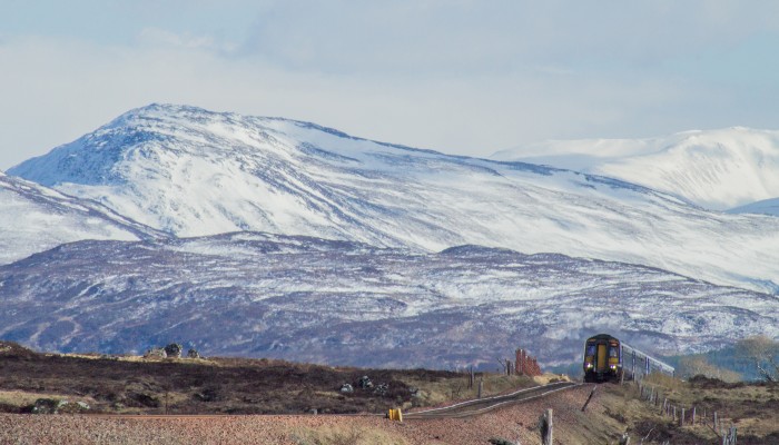 A remote moorland scene with snowcapped hills and a ScotRail train in the distance.