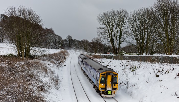 A ScotRail Class 158 train passing through the countryside during winter with snow on the grass and railway tracks.