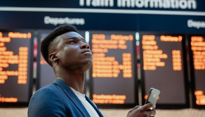 Male standing in front of rail departure boards with his mobile phone