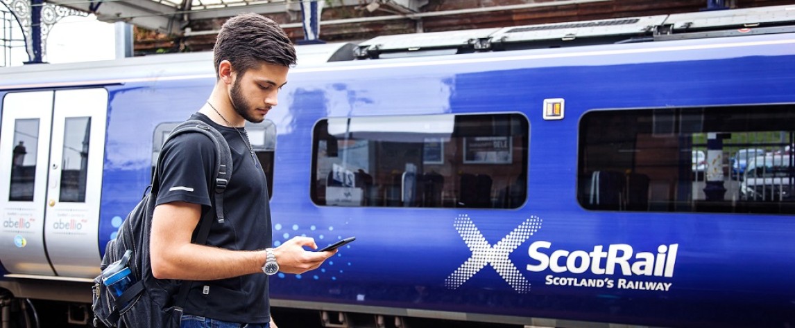 Man using mobile phone, standing beside a ScotRail train