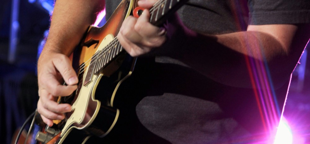 Man in black shirt playing a brown electric guitar